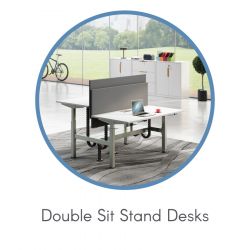 Circular image of double sit-stand desks in a modern, bright office. Desks face each other with a divider; plants and bicycle visible in the background.