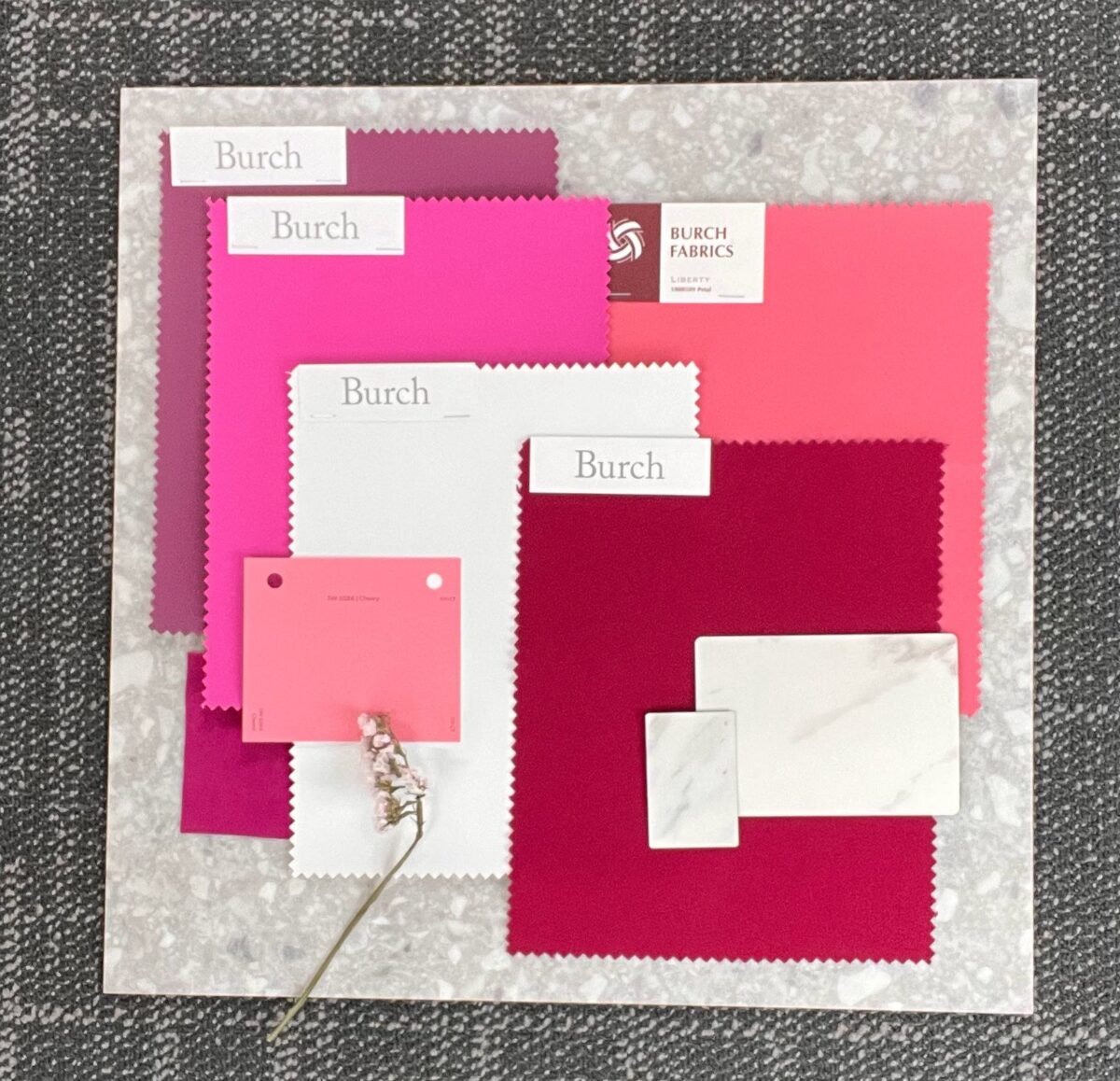 A collage of fabrics and paper samples in pink, red, and white tones on a textured gray background. Labels are placed on some pieces.