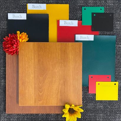 Various colored laminate samples, including wood textures and primary colors, arranged on a dark surface with two vibrant flowers for decoration.