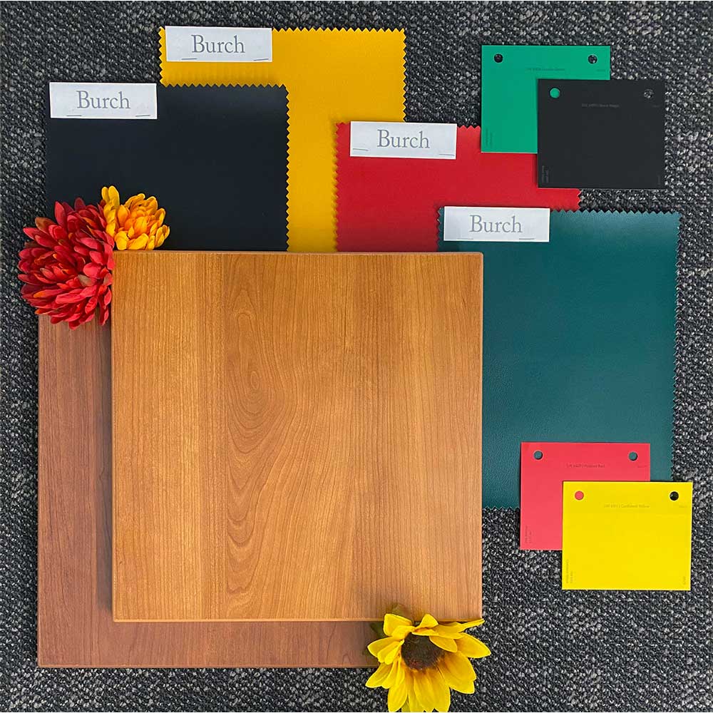 Various colored laminate samples, including wood textures and primary colors, arranged on a dark surface with two vibrant flowers for decoration.