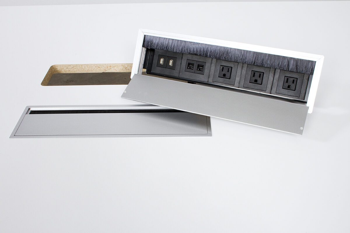 A white wall panel is partially opened, revealing a hidden power outlet strip with multiple sockets inside.