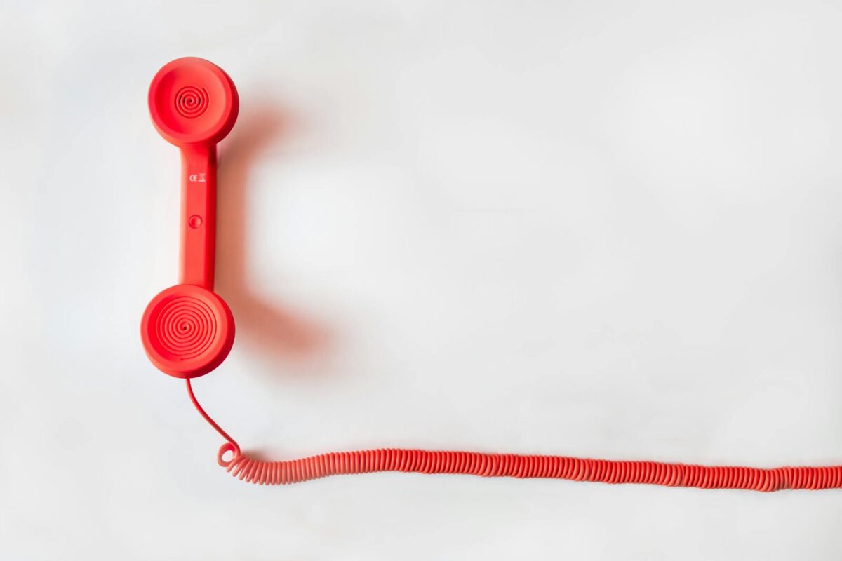 A vintage red rotary telephone receiver with a coiled cord is placed on a plain white background. The minimalistic design suggests nostalgia.