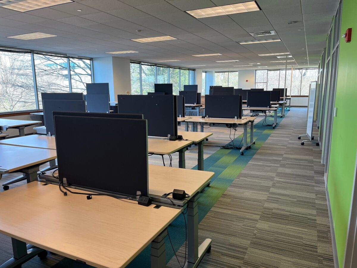 Modern office space with rows of empty desks and computers, large windows letting in natural light, and a calm, organized atmosphere.
