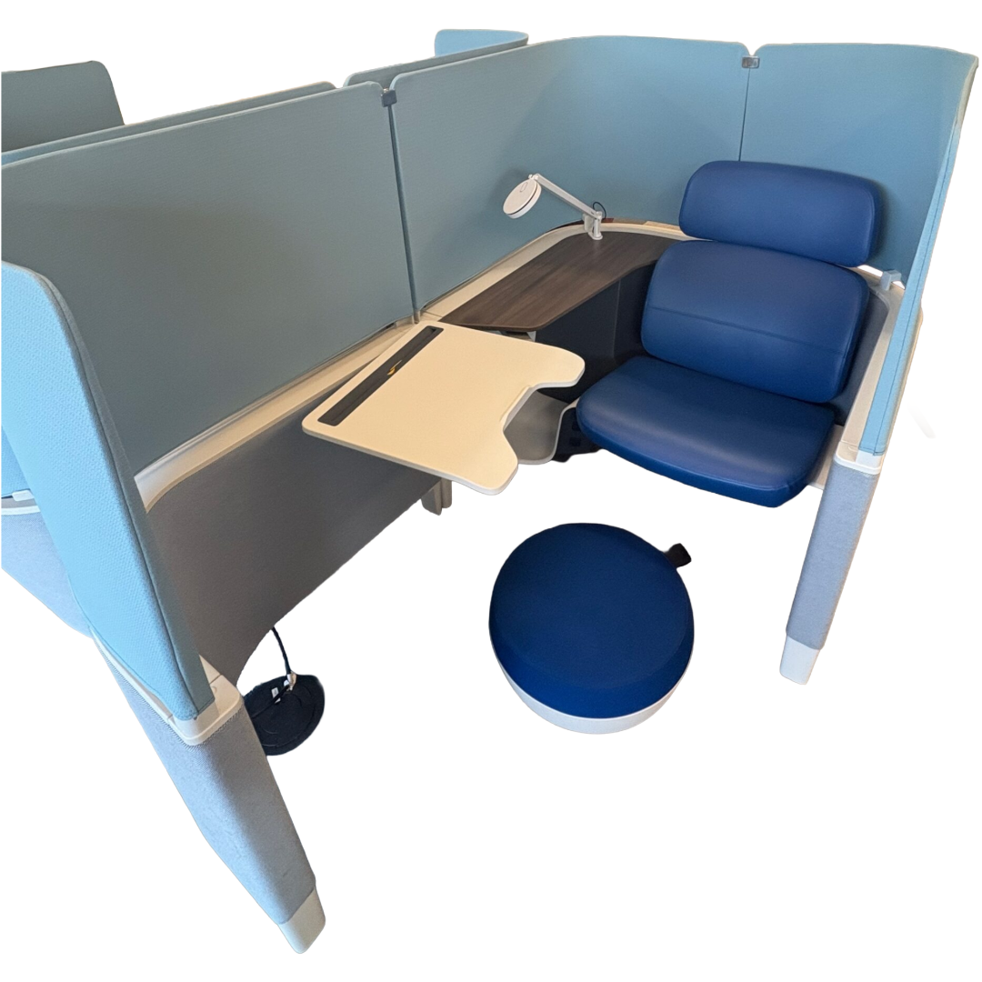 A modern workspace pod with blue cushioned seating, a white adjustable desk, and a small lamp. Blue privacy panels surround the compact area.