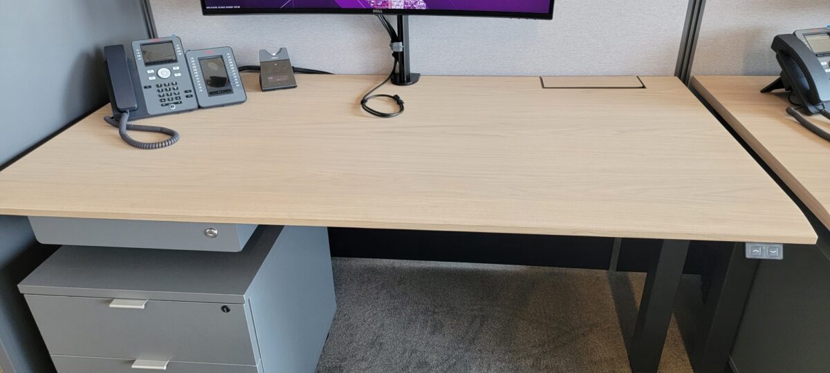 Height adjustable desk with light wood laminate worksurface and white base clean ergonomic office workstation setup at Conklin Office Furniture